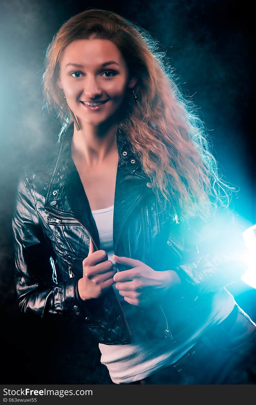 Portrait of amazing young woman with curly blond hair dressed in stylish black jacket. Over blue color spotlight. Portrait of amazing young woman with curly blond hair dressed in stylish black jacket. Over blue color spotlight.