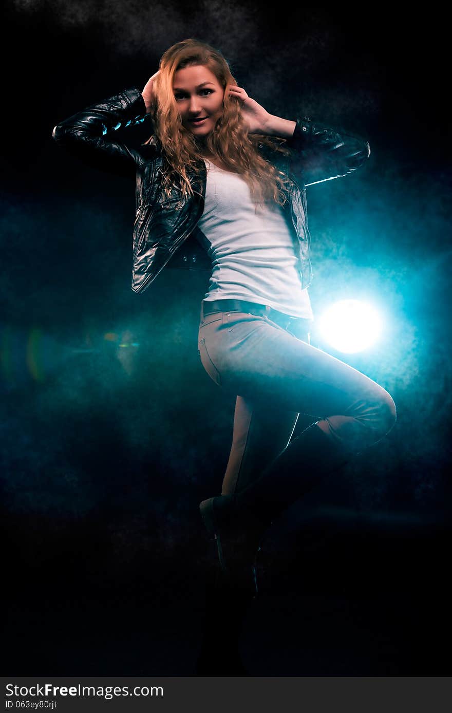 Portrait of amazing young woman with curly blond hair dressed in stylish black jacket. Over blue color spotlight. Portrait of amazing young woman with curly blond hair dressed in stylish black jacket. Over blue color spotlight.