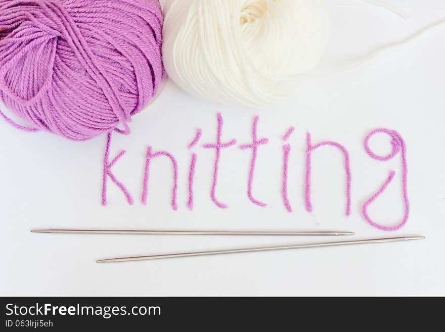 Written knitting with violet yarn, white and violet woolen skeins and knitted pieces.