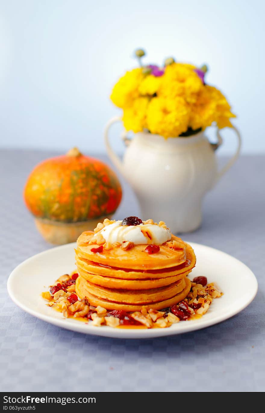 A stack of pumpkin pancakes with walnuts, cranberries, honey and yogurt