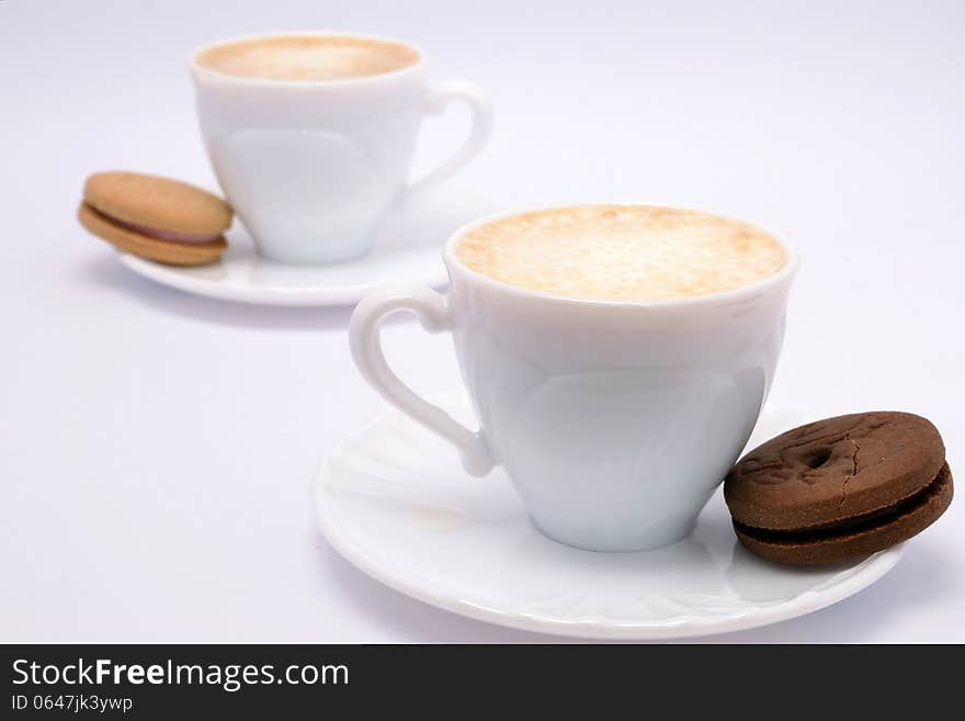 Coffee with milk and cream in beautiful fine china cups accompanied by vanilla and chocolate cookies. Coffee with milk and cream in beautiful fine china cups accompanied by vanilla and chocolate cookies