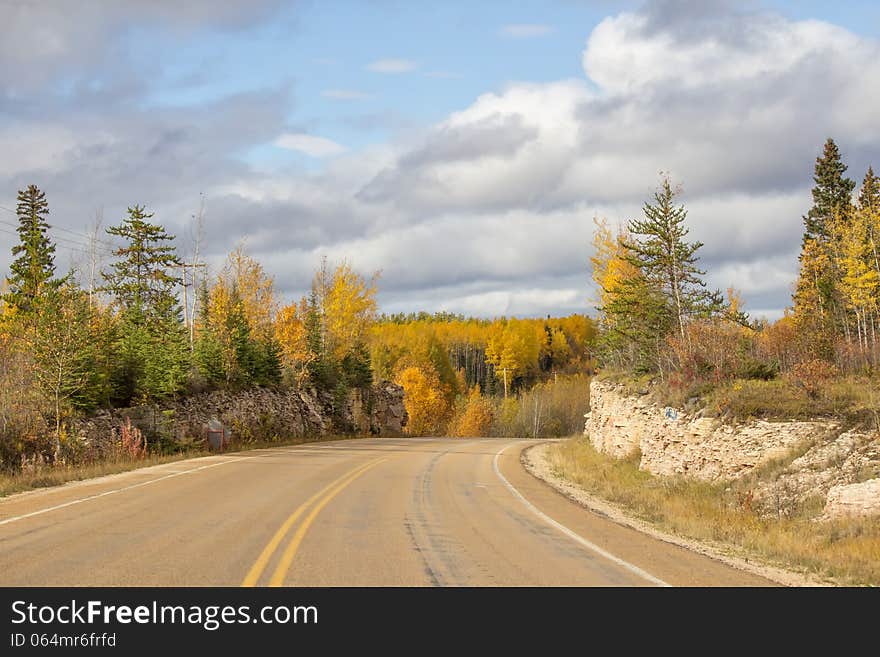 Winding highway between a rock ridge and trees