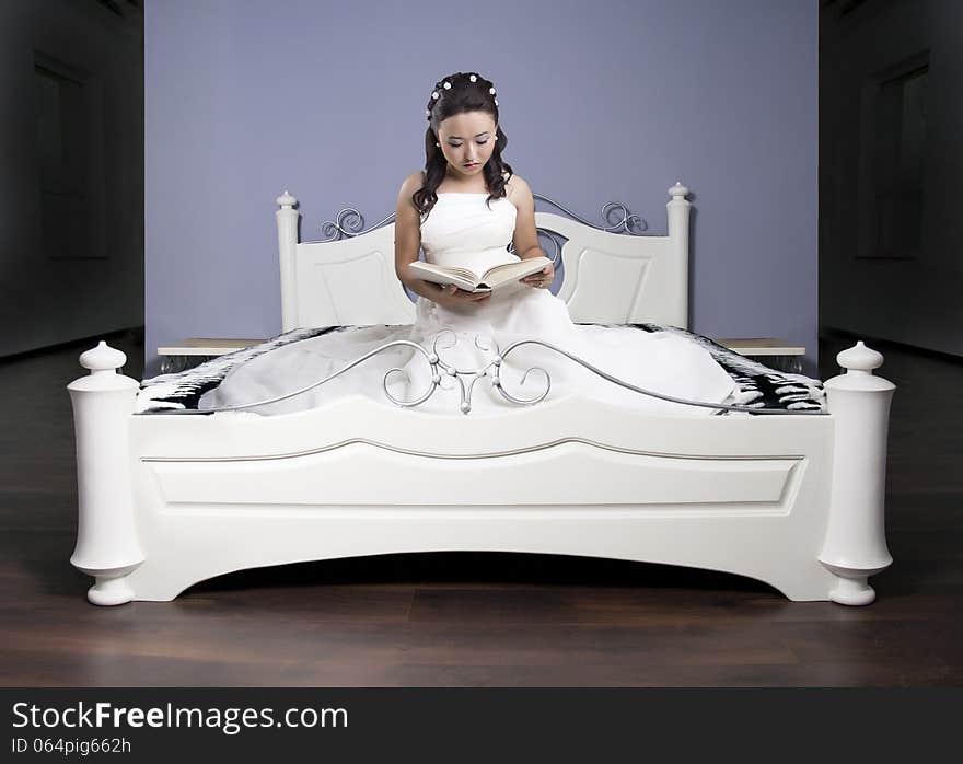 Girl in a long dress on a white bed reads the book. Girl in a long dress on a white bed reads the book