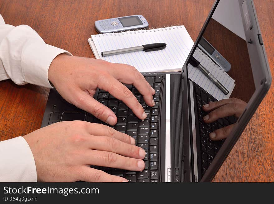 Hands working on a laptop in the office plus a black pen and a mobile. Hands working on a laptop in the office plus a black pen and a mobile