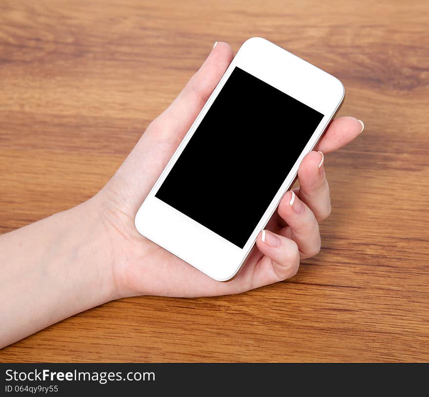 Woman hand holding a touch white phone with black screen against the background of a wooden table. Woman hand holding a touch white phone with black screen against the background of a wooden table