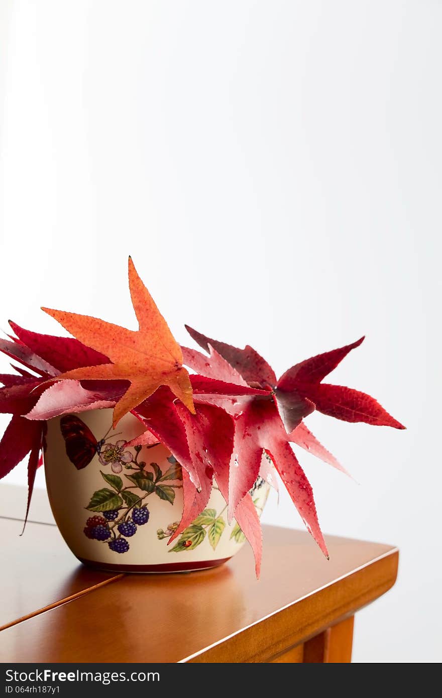 Ceramic vase with autumn leaves stands on the corner table white background. Ceramic vase with autumn leaves stands on the corner table white background