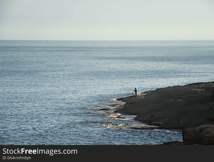 One fisherman on the rock fishing early morning with dusk and dirty sky background, dirty morning light and alone fisherman fishing in the sea, selective focus to the man, solitude, calm morning