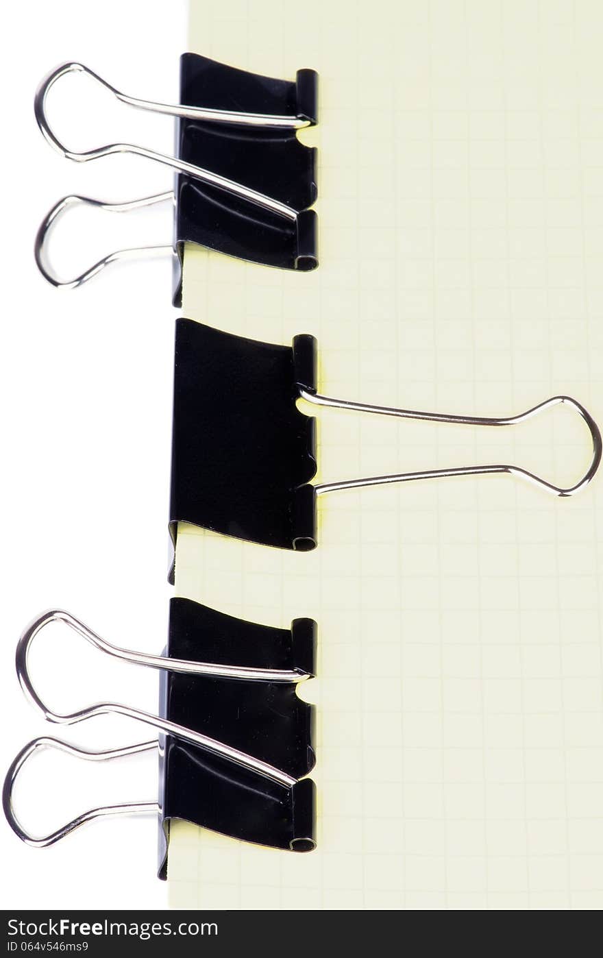 Black Metal Paper Clip In a Row on Checkered Yellow Paper isolated on white background. Black Metal Paper Clip In a Row on Checkered Yellow Paper isolated on white background