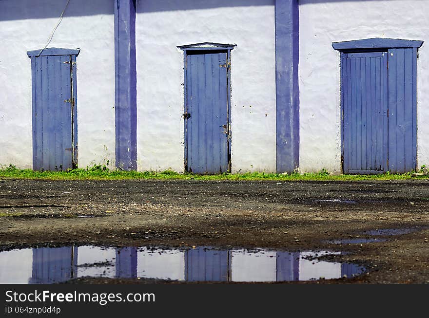 Three old purple doors and puddle reflection.