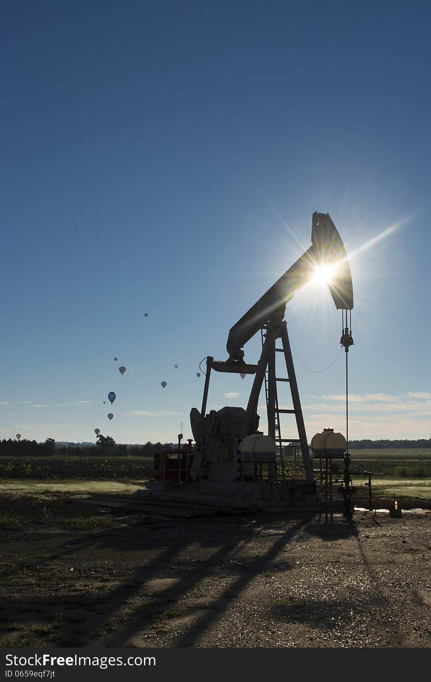 Silhouette of a petroleum oil pumping unit with hot air balloons flying in the distance. Silhouette of a petroleum oil pumping unit with hot air balloons flying in the distance