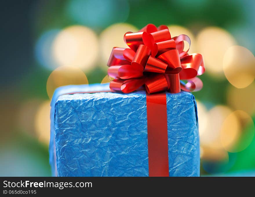 A blue gift with a red ribbon on Christmas bokeh background