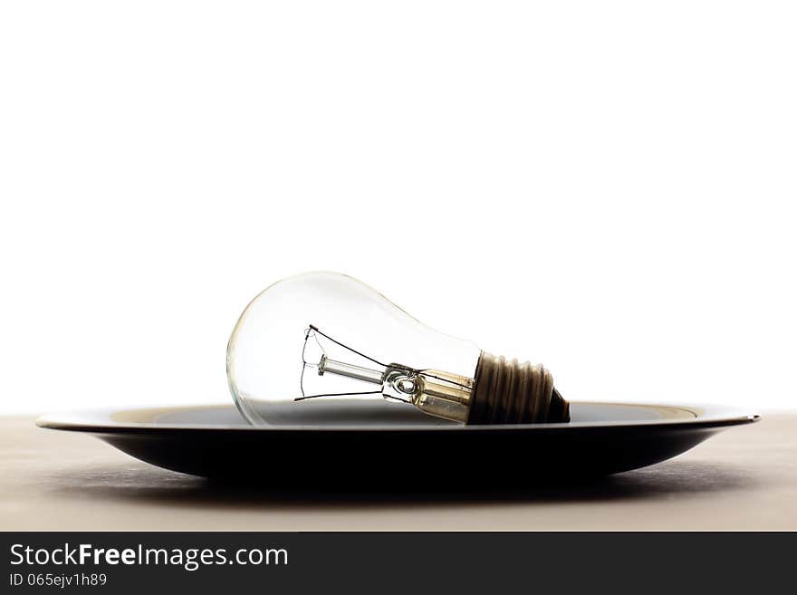 Light bulb served in black plate on table, white background