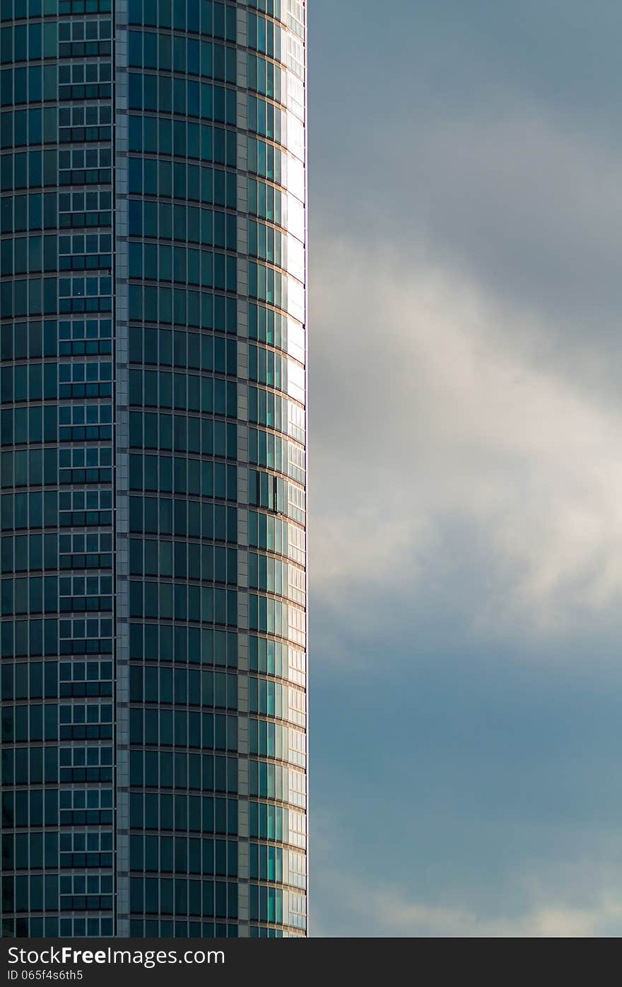 Rounded Tall Skyscraper with Green Glass against Cloudy Stormy Sky. Rounded Tall Skyscraper with Green Glass against Cloudy Stormy Sky