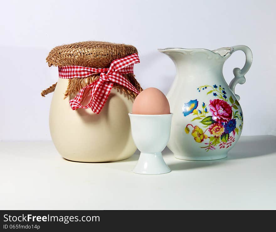 An arrangement of a jar, pitcher and egg in egg cup on white background. An arrangement of a jar, pitcher and egg in egg cup on white background