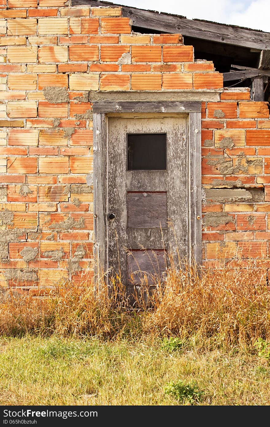 A dilapidated brick wall that's crumbling with a weathered grey door. A dilapidated brick wall that's crumbling with a weathered grey door