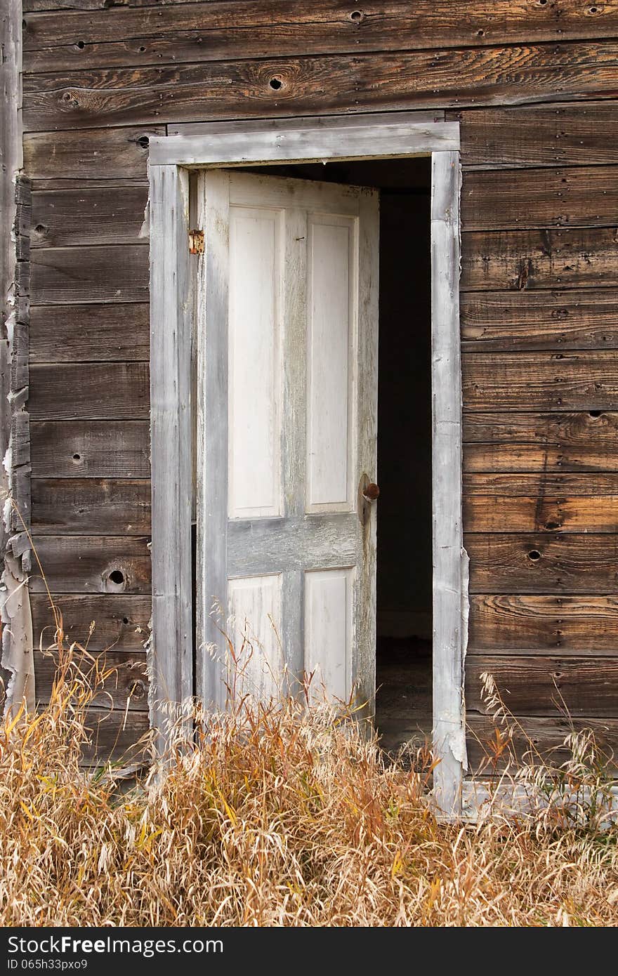 A white wood door standing ajar surrounded by weathered dark brown wood boards