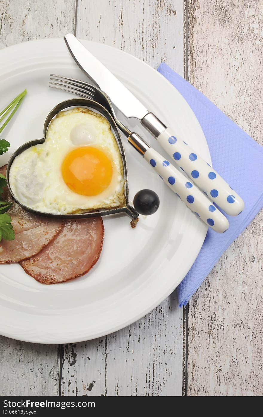 Modern breakfast of Ham with heart shape egg cooked breakfast on modern vintage shabby chic blue table with polka dot cutlery. Modern breakfast of Ham with heart shape egg cooked breakfast on modern vintage shabby chic blue table with polka dot cutlery.