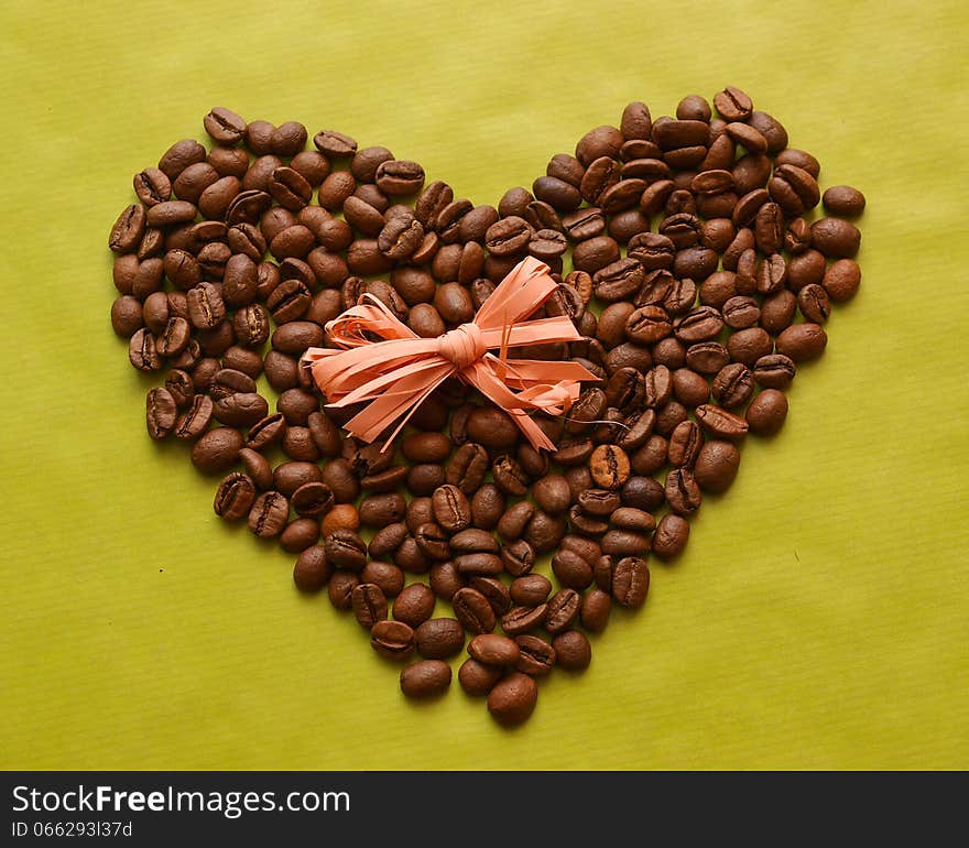 Photo of coffee beans in a shape of heart with a bow on green background