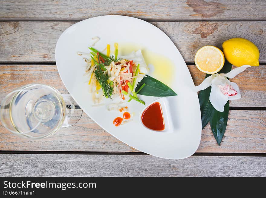 Serving of steamed sea bass fillet on a plate in a restaurant, on a wooden table with white wine and decor. Serving of steamed sea bass fillet on a plate in a restaurant, on a wooden table with white wine and decor