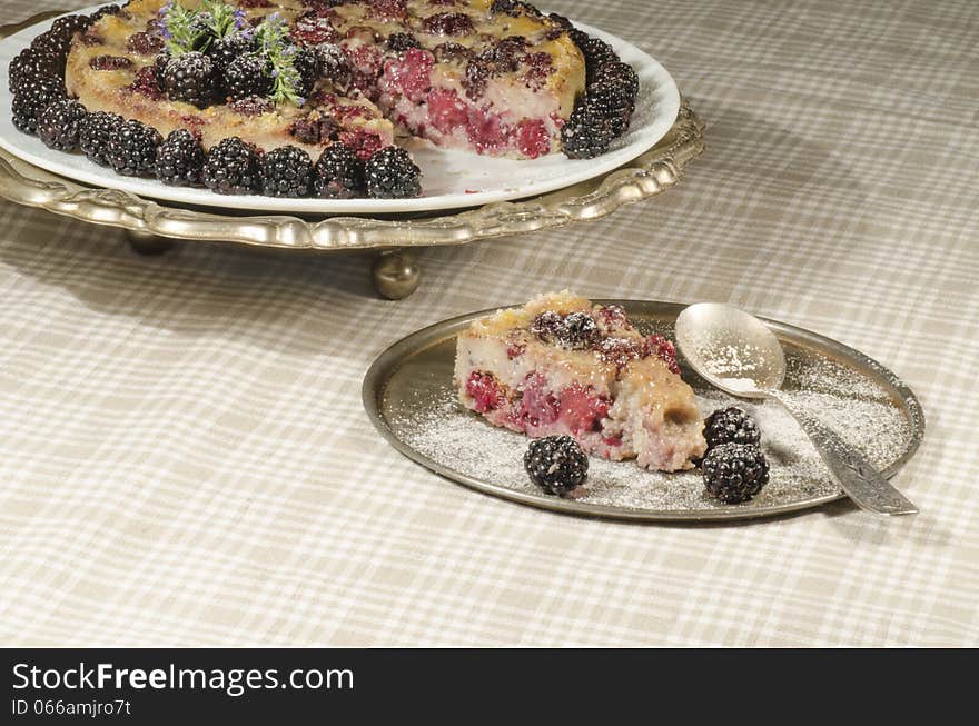 Slice of Blackberry Clafoutis on metal plate with fresh berries