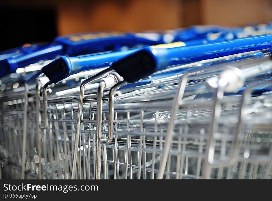 Close up of a row of empty metal shopping carts with blue handles in a supermarket. Close up of a row of empty metal shopping carts with blue handles in a supermarket