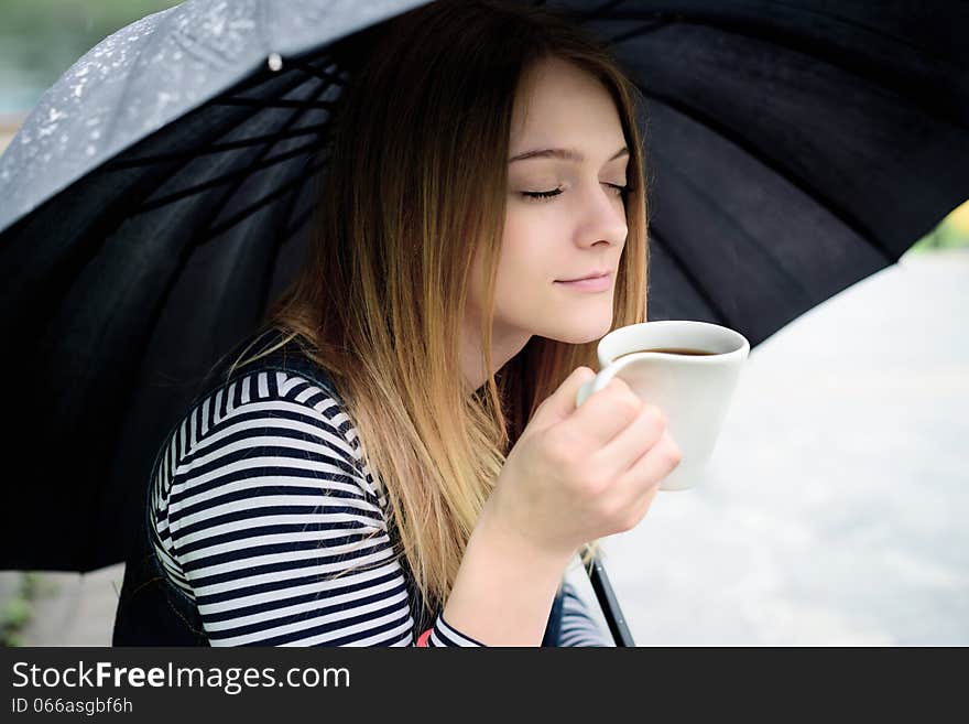 Womanl drinks fragrant coffee with pleasure under umbrella in bad weather