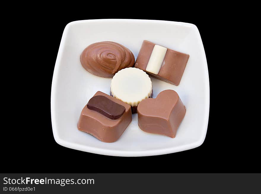 Cut-out of a variety of chocolates in a white plate over black background.