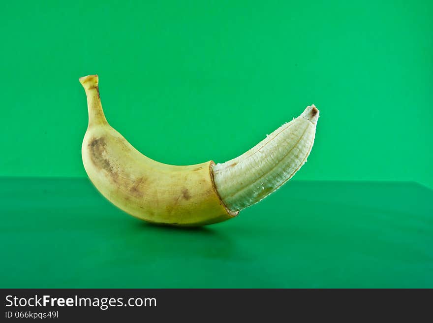 Banana half peeled lies against a green background. Banana half peeled lies against a green background