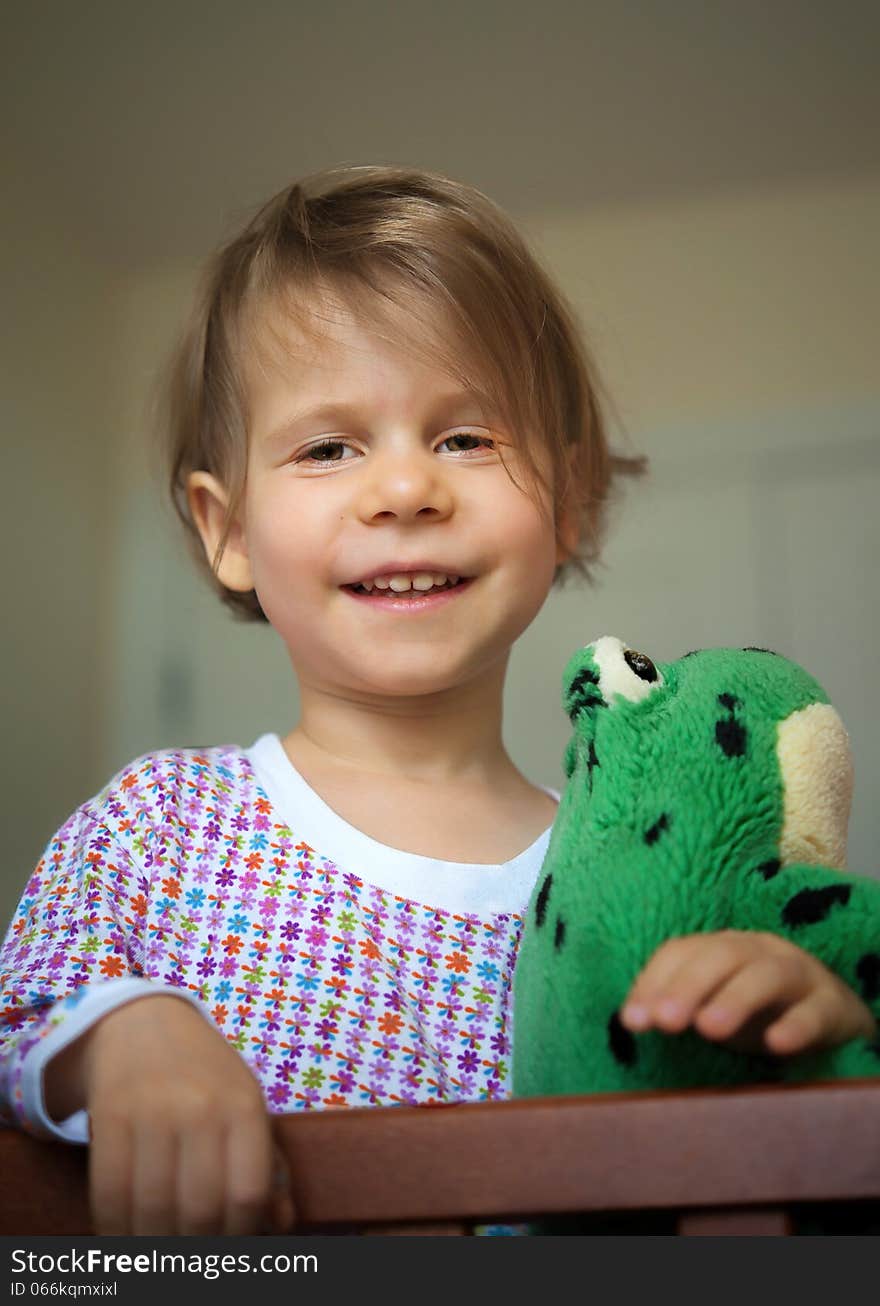 Cheerful little girl woke up in the morning, standing in the crib and keeps her toy. Cheerful little girl woke up in the morning, standing in the crib and keeps her toy