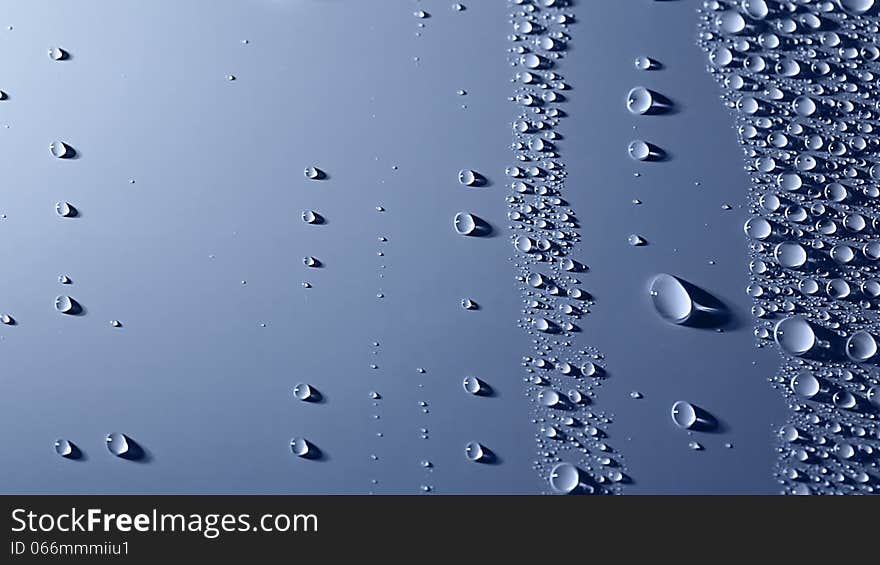 A lot of water drops are on the blue background. Oblique illumination. Shadows. Two large drops slowly slide down one after another. A lot of water drops are on the blue background. Oblique illumination. Shadows. Two large drops slowly slide down one after another