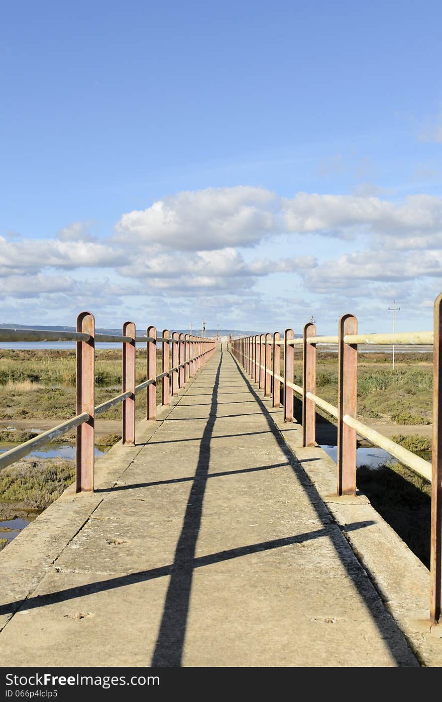 A bridge crosses the lagoon and marshes to reach the sea. in the background blue sky with clouds. A bridge crosses the lagoon and marshes to reach the sea. in the background blue sky with clouds.