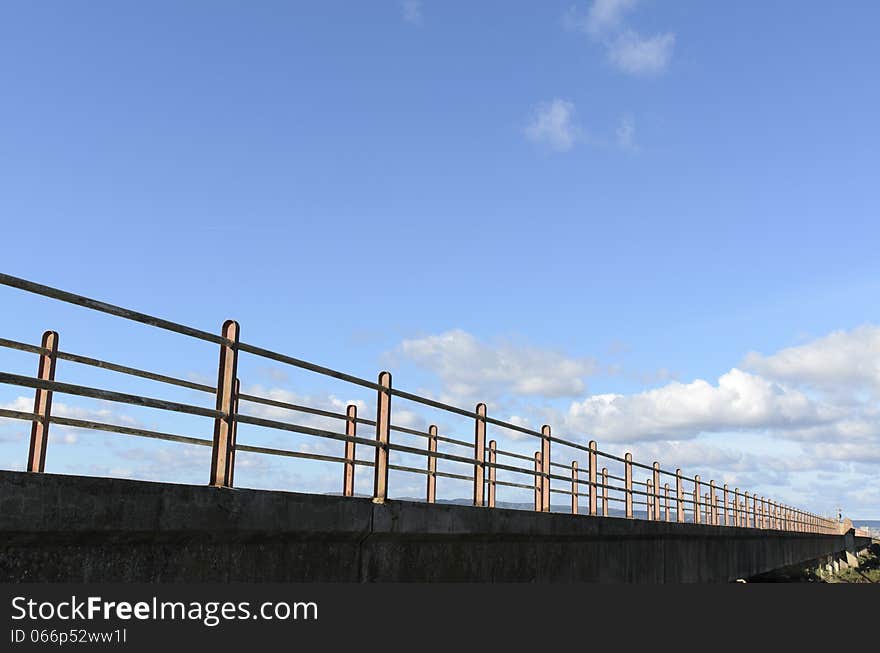 A bridge crosses the lagoon and marshes to reach the sea. in the background blue sky with clouds. A bridge crosses the lagoon and marshes to reach the sea. in the background blue sky with clouds.