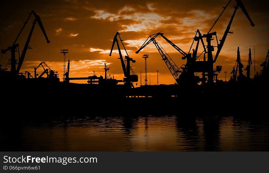 Evening. The last rays of sunshine through the clouds. Seaport. Cranes are working. Silhouettes. Evening. The last rays of sunshine through the clouds. Seaport. Cranes are working. Silhouettes