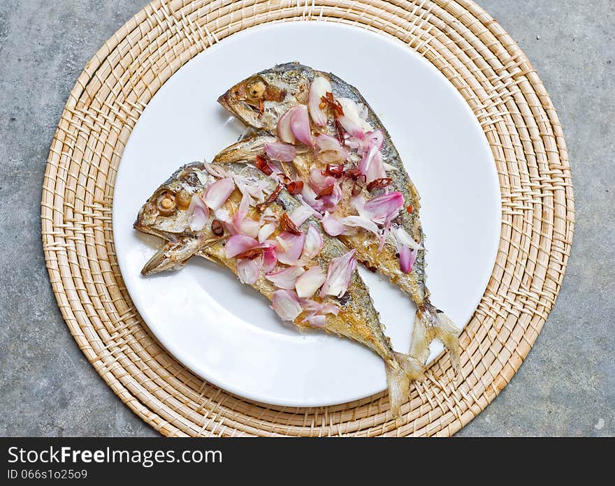 Deep fry two mackerel fish topping with sliced shallot and chilli on white plate. Deep fry two mackerel fish topping with sliced shallot and chilli on white plate