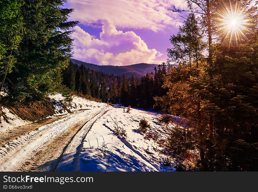 Winter mountain landscape. winding road that leads into the pine forest covered with snow. wooden fence stands near the road. Winter mountain landscape. winding road that leads into the pine forest covered with snow. wooden fence stands near the road.