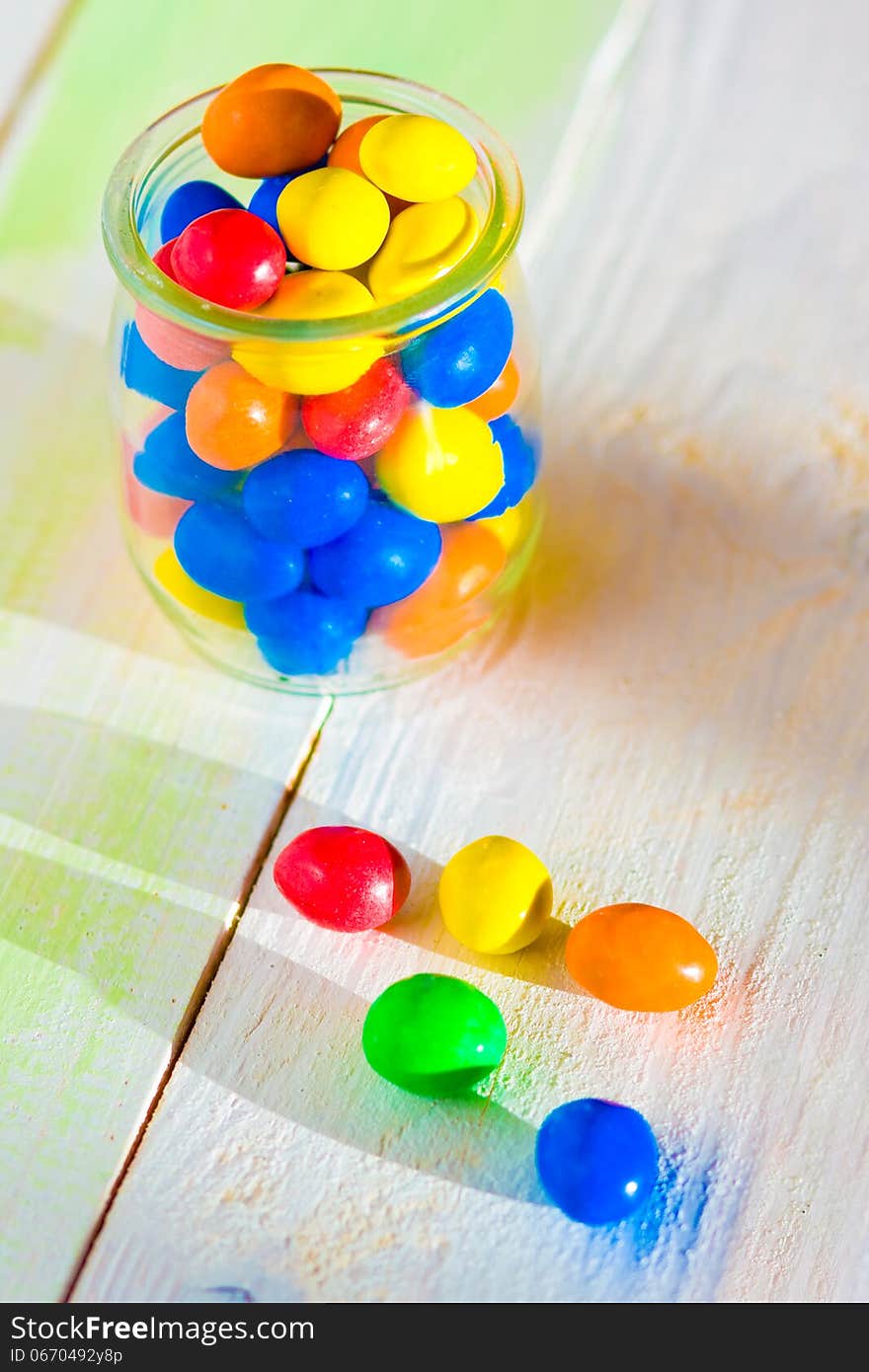 Colored candy in glass jar on wooden background