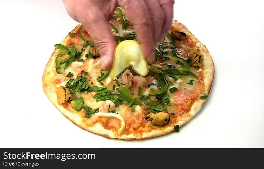 Men's hand to squeeze the lemon on the pizza with seafood (shrimp, mussels), and pepper, cheese on a white background