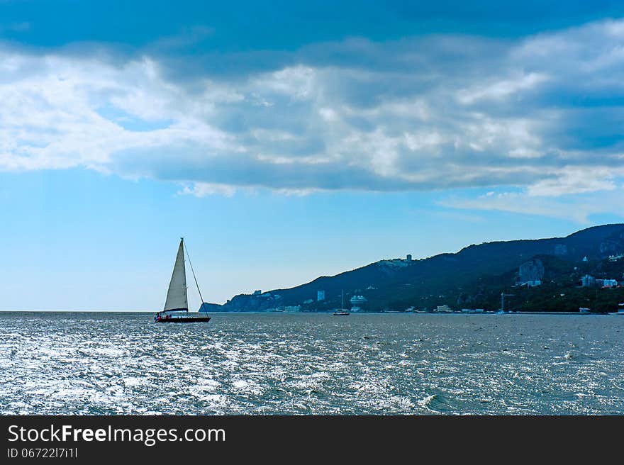 Yacht and blue water ocean. Shore the background. Yacht and blue water ocean. Shore the background