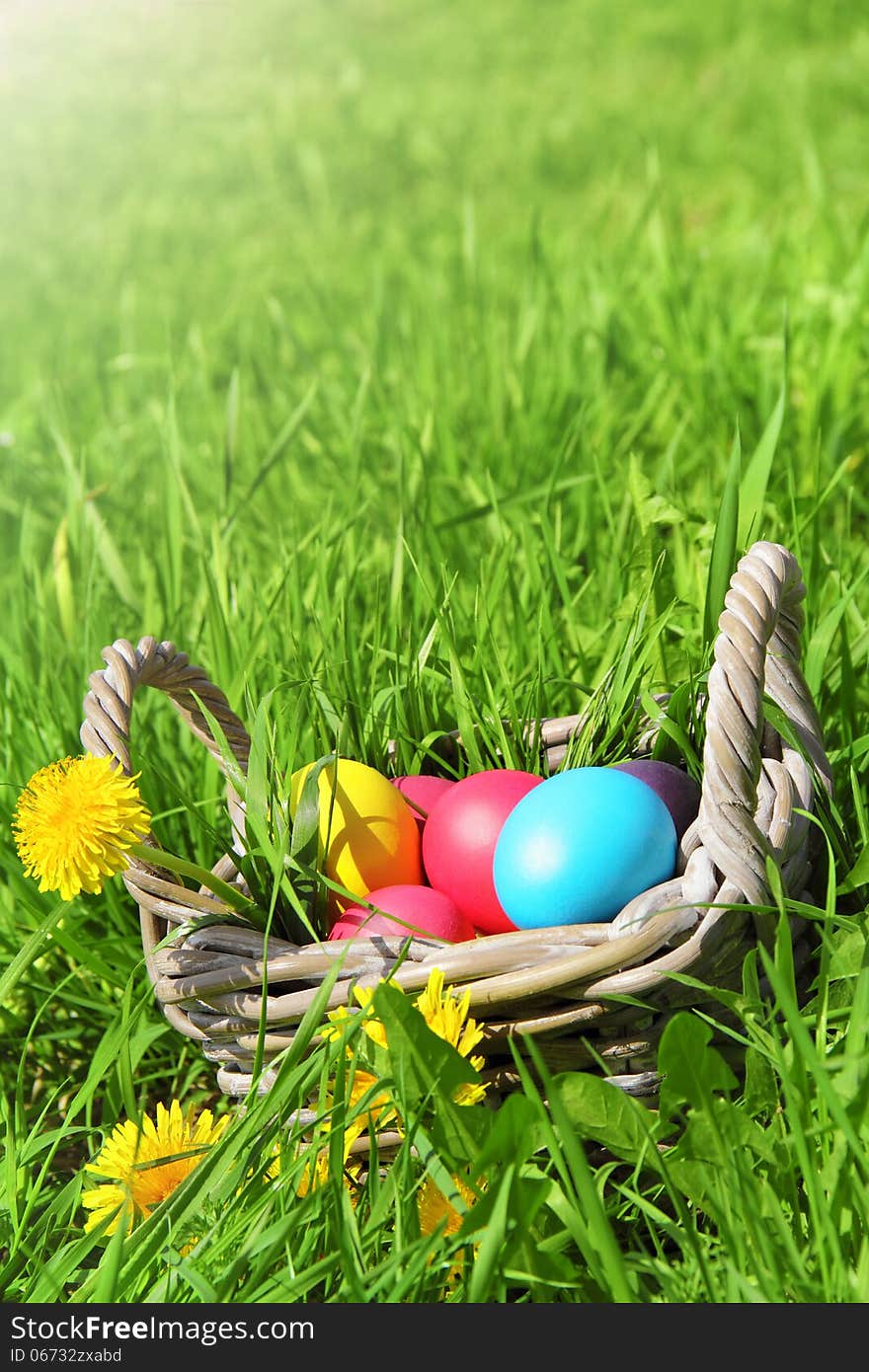 Wicker basket with Easter eggs and flowers in the grass