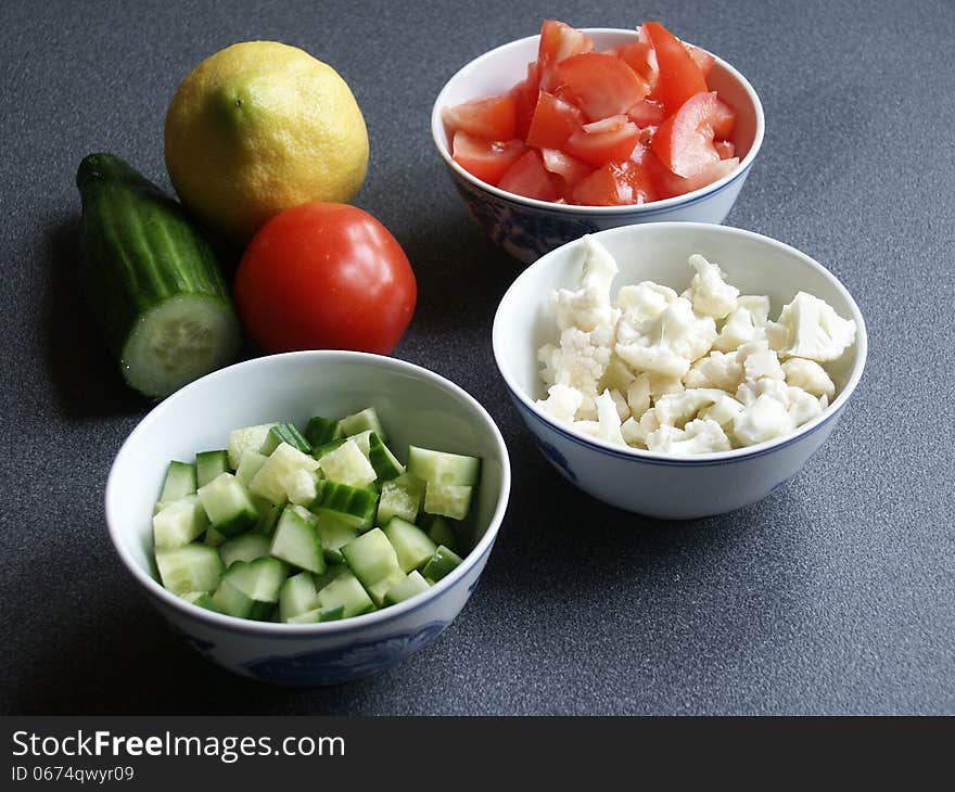 Tomato, cauliflower, and cucumber in three blue bowls on blue background. There is a whole tomato, cucumber, and lemon in the picture too. Tomato, cauliflower, and cucumber in three blue bowls on blue background. There is a whole tomato, cucumber, and lemon in the picture too.