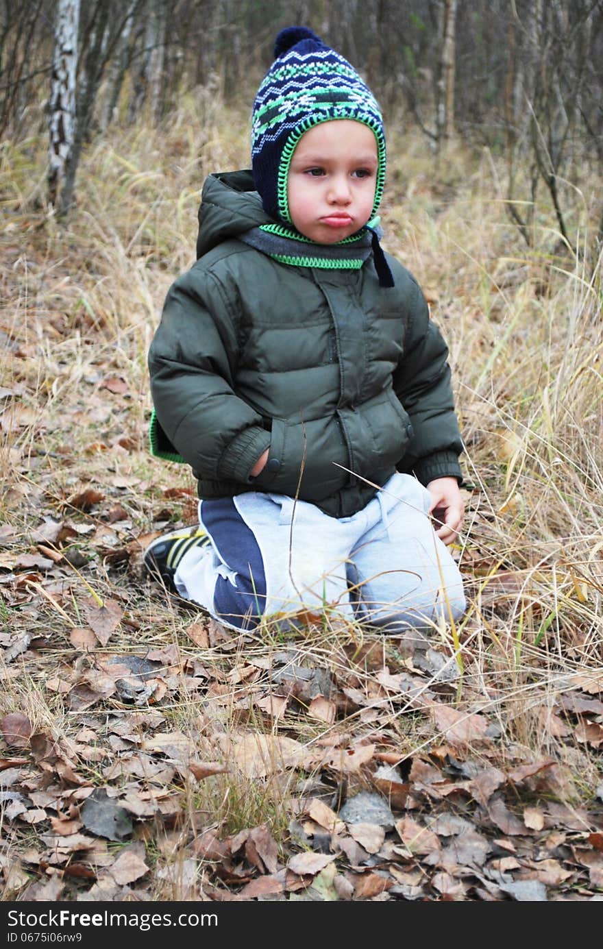 In the autumn forest sitting on the grass sad upset boy