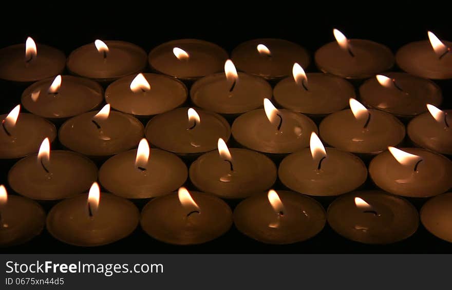 Flame (fire) of many candles vibrate on a wind. A black background