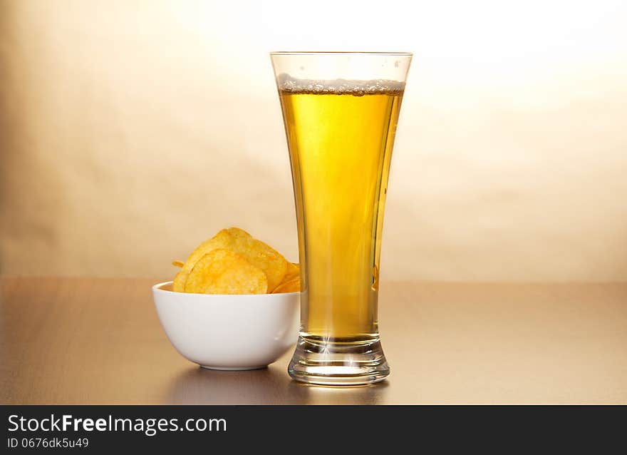 Glass of light beer and bowl with chips against paper