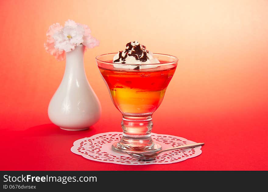 Glass with a dessert, a teaspoon, a napkin and a vase with the flowers on a pink background. Glass with a dessert, a teaspoon, a napkin and a vase with the flowers on a pink background