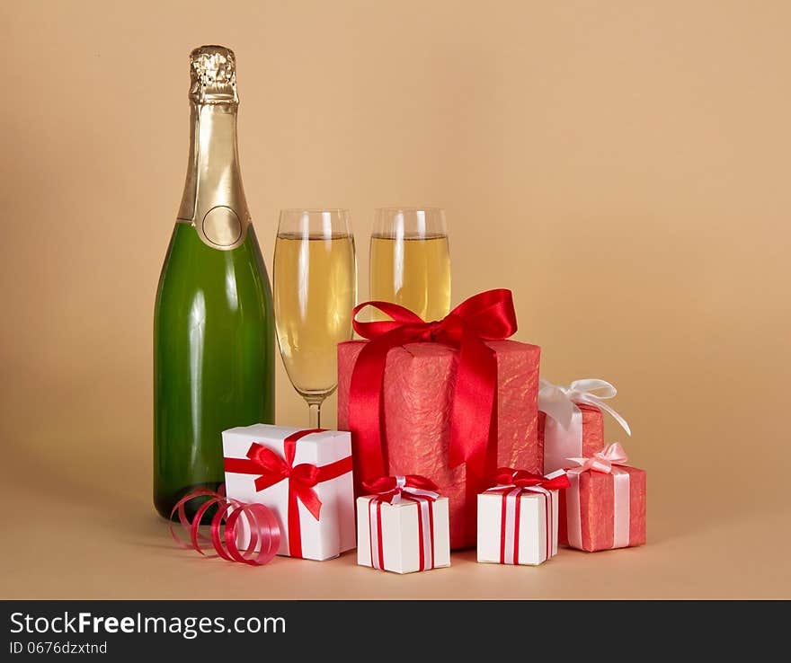 Bottle and wine glasses with champagne, big and small gift boxes on a beige background. Bottle and wine glasses with champagne, big and small gift boxes on a beige background