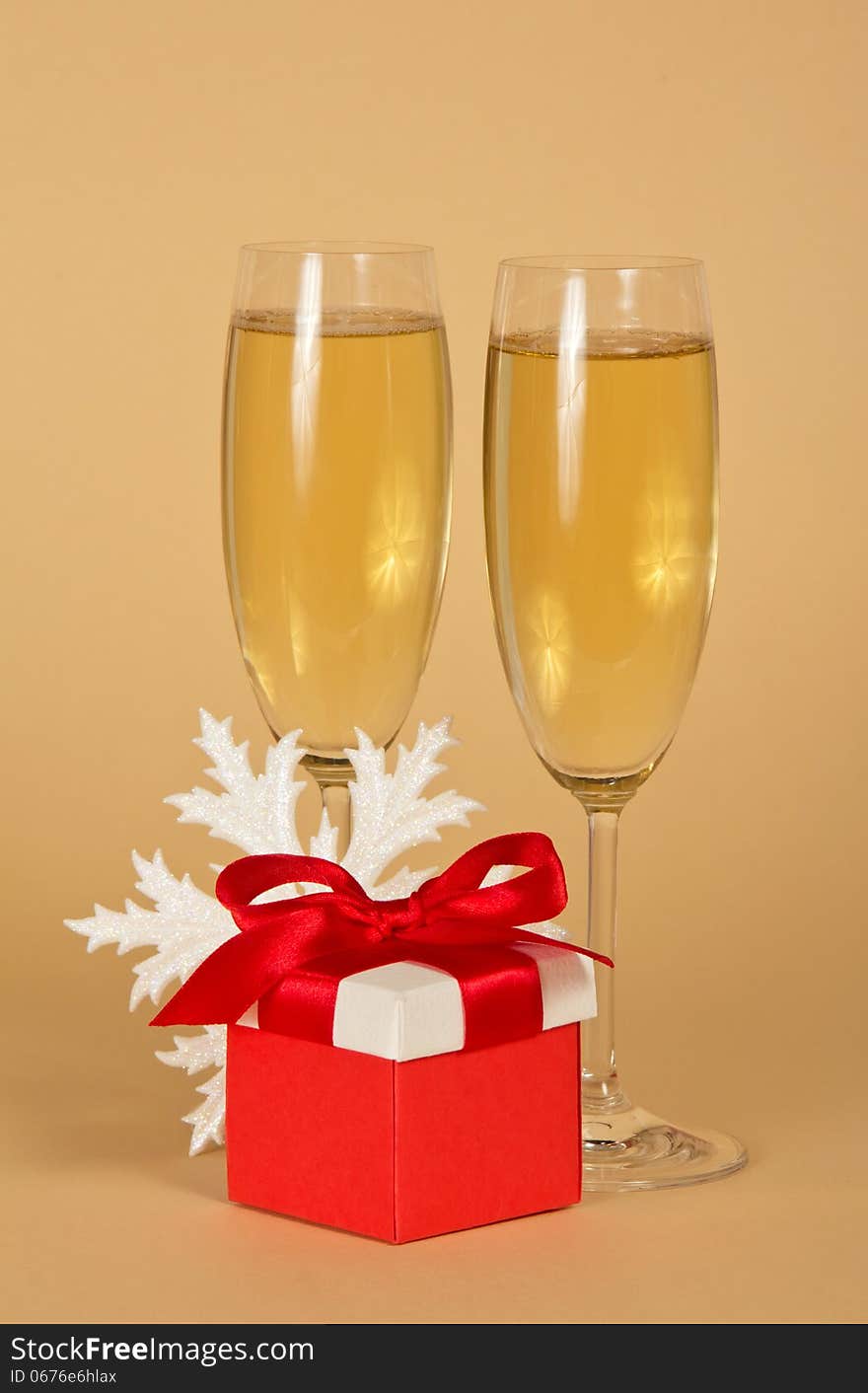 Wine glasses with champagne, a red gift box with a bow and a snowflake on a beige background