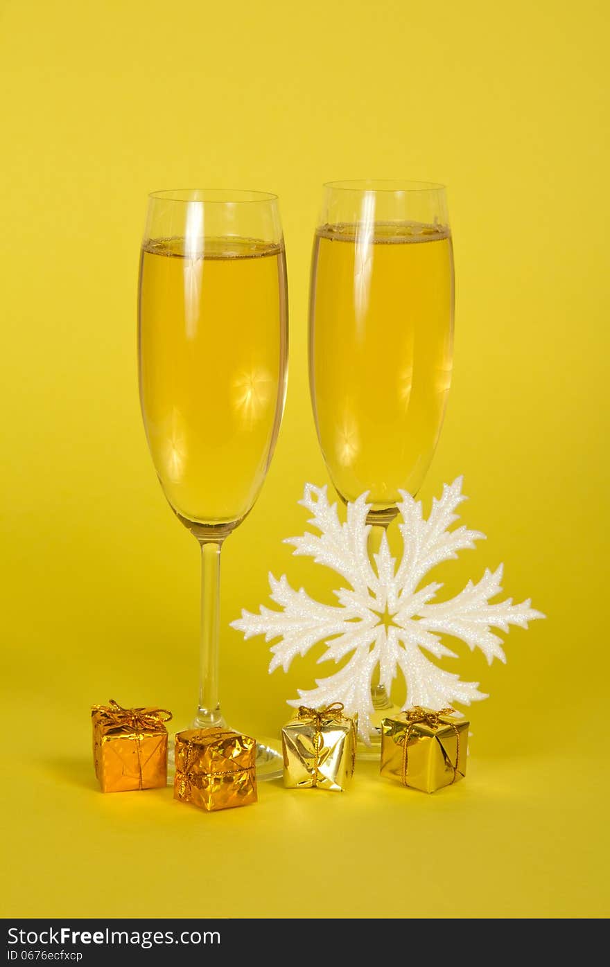 Christmas champagne in wine glasses small gift boxes and a snowflake on a yellow background