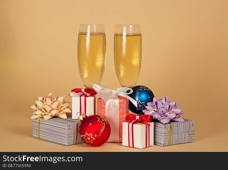 Two wine glasses with champagne, charming gift boxes and Christmas toys on a beige background