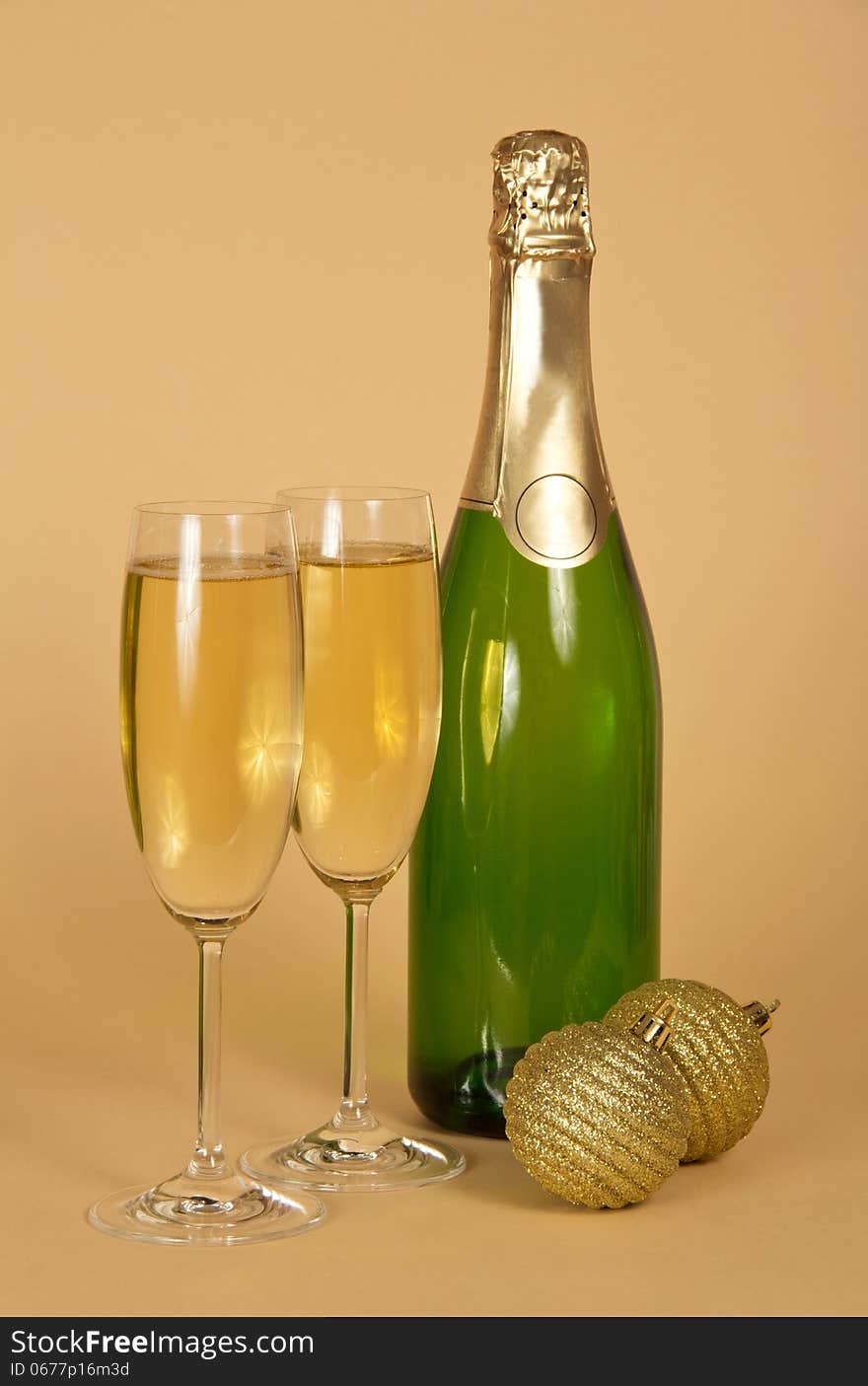 Bottle and two wine glasses with champagne, two golden New Year's balls on a beige background