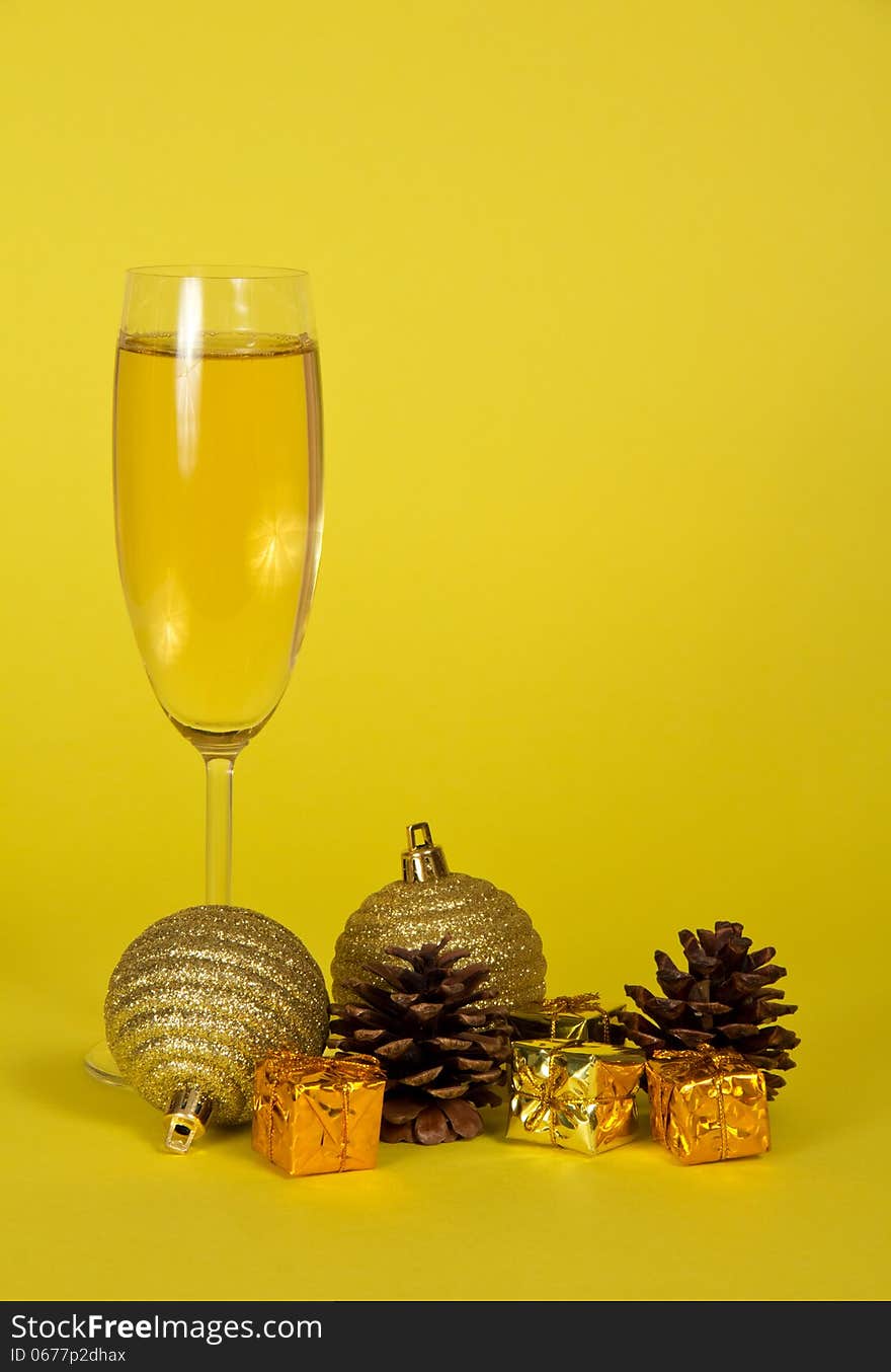 Champagne wine glass, small gift boxes, Christmas toys and pine cones on a yellow background